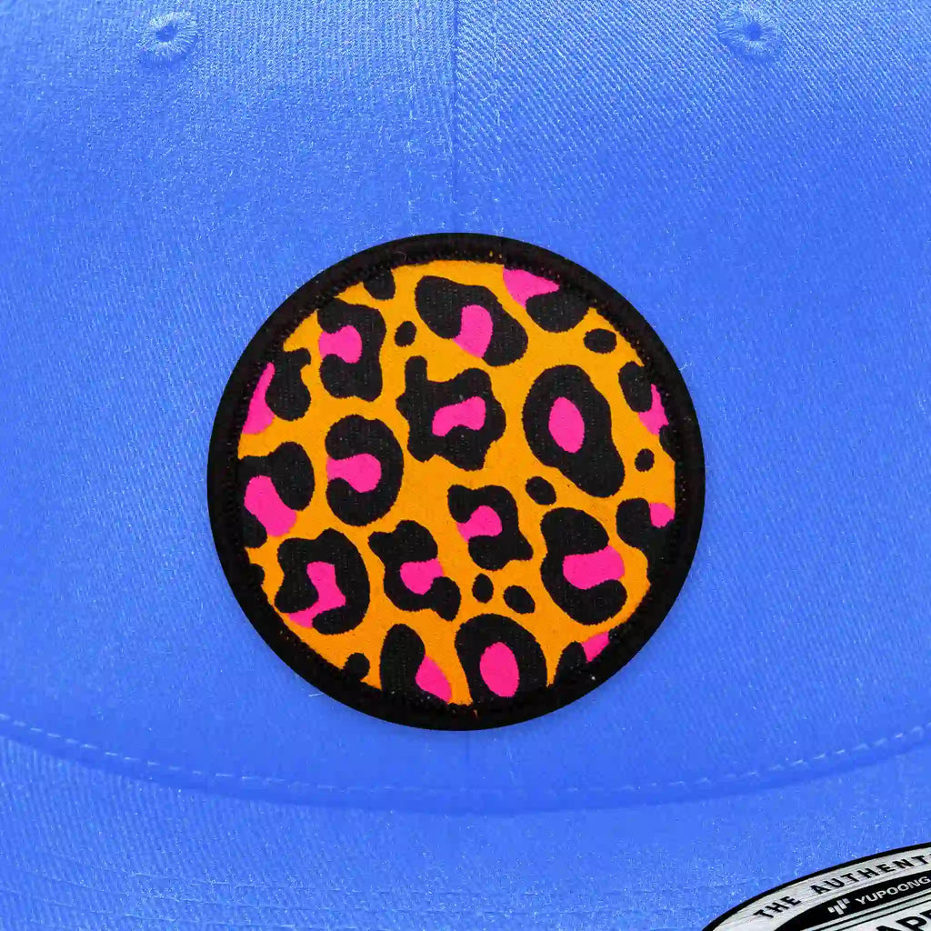 Casquette Flexfit bleu clair ornée d’un écusson velcro imprimé motif léopard orange et rose, mode urbaine et décontractée.