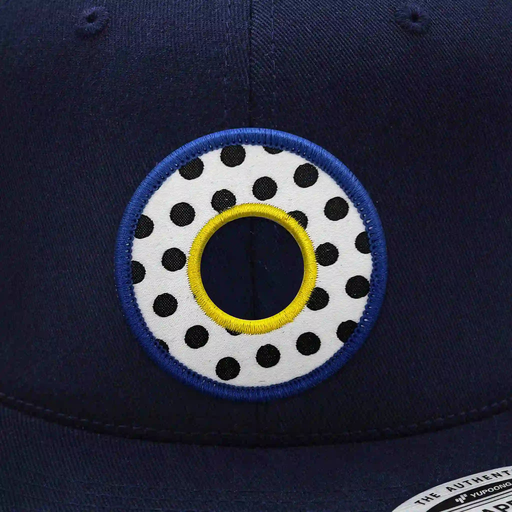 Casquette Flexfit bleue navy snapback avec écusson rond blanc à pois noirs style Memphis, cerclé de bleu et jaune, modèle urbain et personnalisable avec velcro et écussons interchangeables.