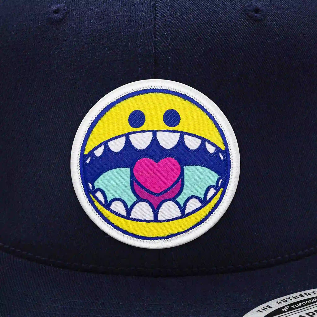 Casquette Flexfit bleue navy snapback avec écusson rond smiley jaune à bouche ouverte et cœur rose, casquette urbaine personnalisable avec velcro et écussons interchangeables.
