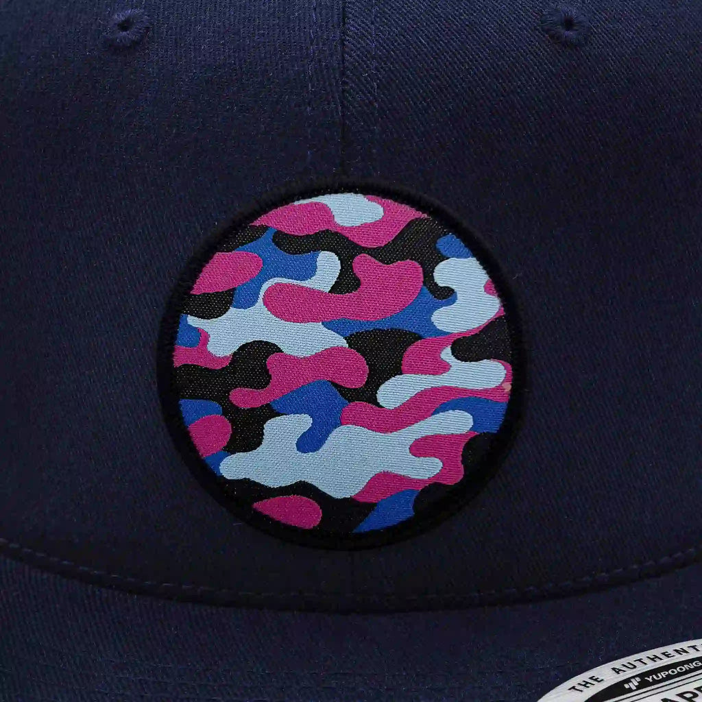 Casquette Flexfit navy snapback avec écusson rond velcro imprimé camouflage bleu, rose et noir, modèle streetwear personnalisable avec écussons interchangeables.