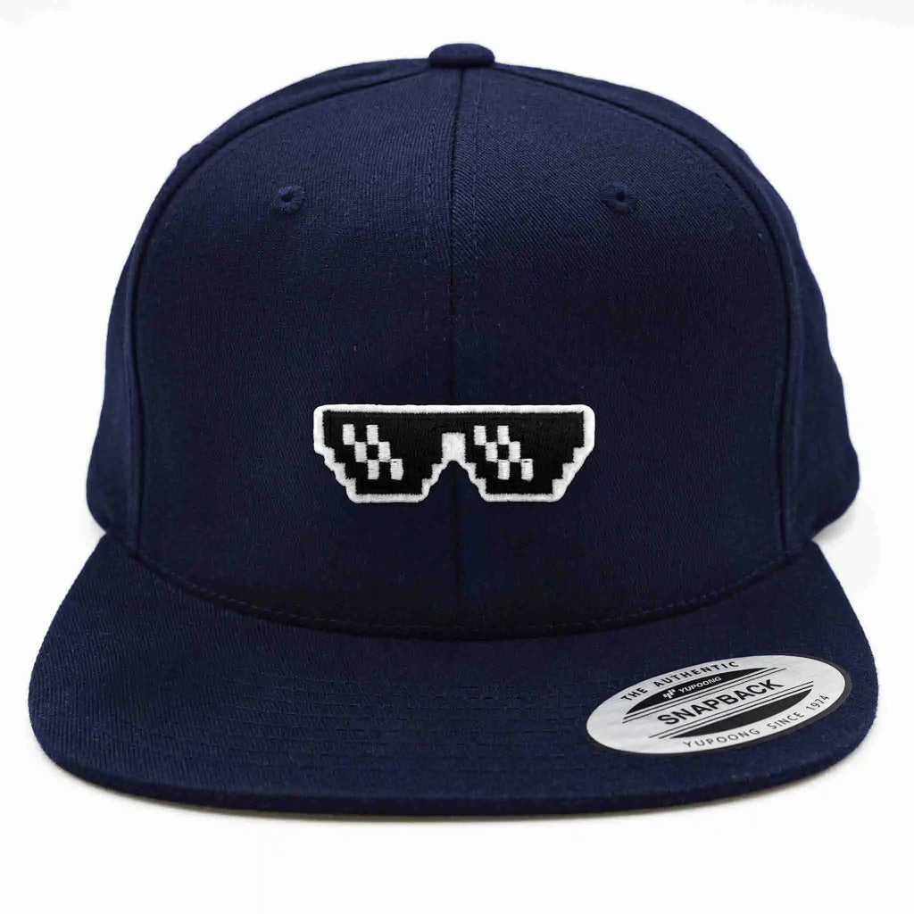 Casquette Flexfit bleue marine snapback avec écusson brodé en forme de lunettes pixel noires et blanches style “Thug Life”, modèle streetwear personnalisable avec velcro et écussons interchangeables.