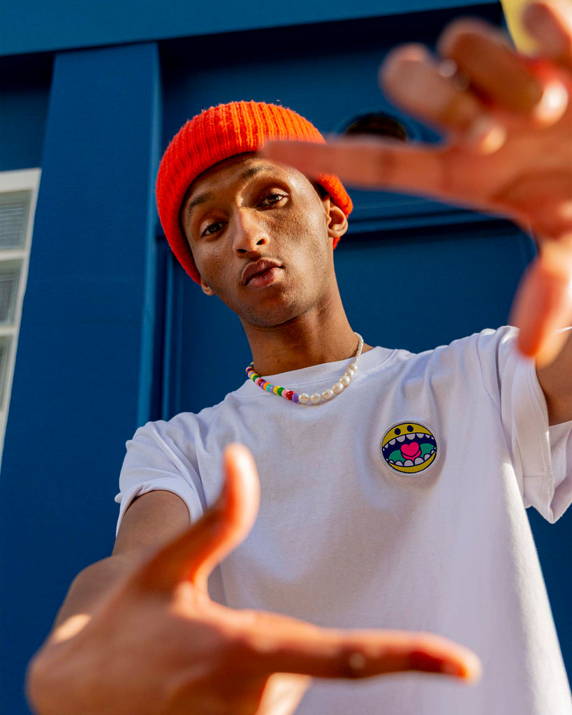 Modèle mode en t-shirt blanc uni avec écusson smiley, lumière naturelle et composition épurée.