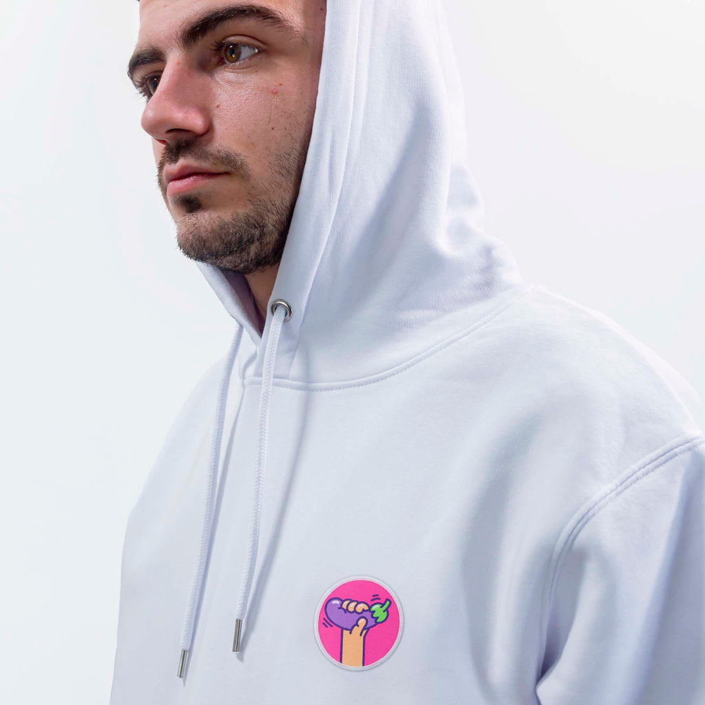 Homme en hoodie blanc portant un écusson aubergine rond et coloré, style patch thermocollant ou scratch.