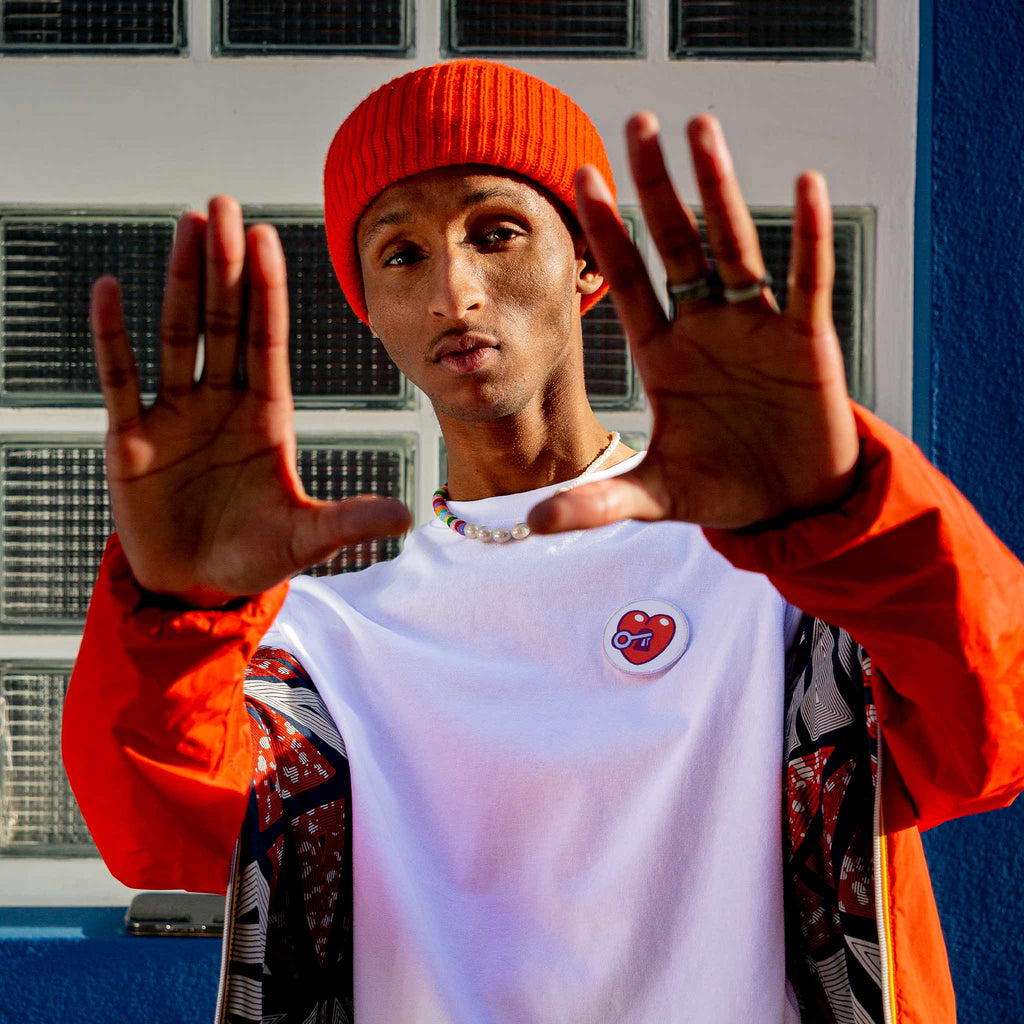 Homme portant un t-shirt blanc décoré d’un écusson scratch en forme de cœur rouge, style coloré et urbain