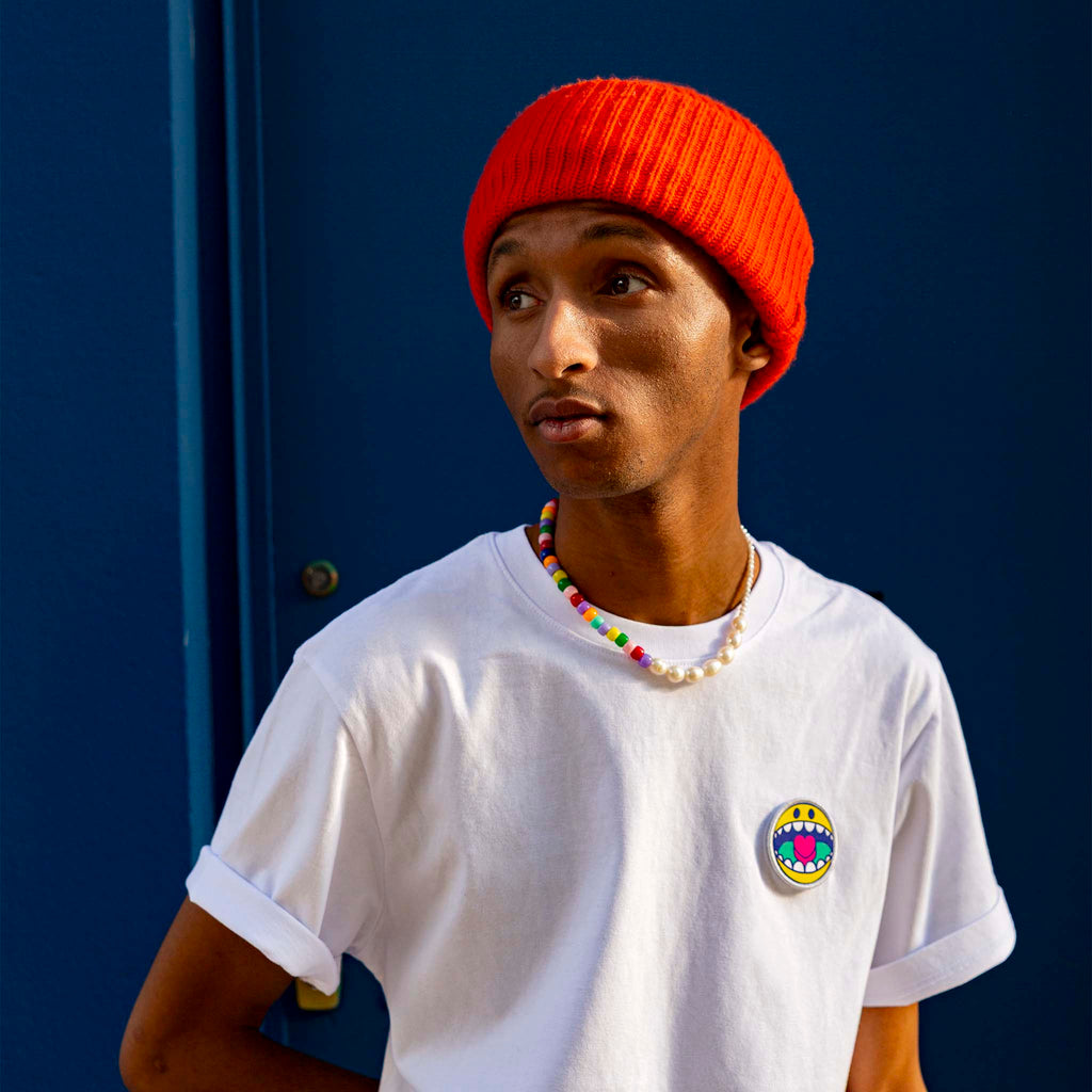 Silhouette posée en t-shirt blanc avec écusson smiley brodé, ambiance studio contemporaine.