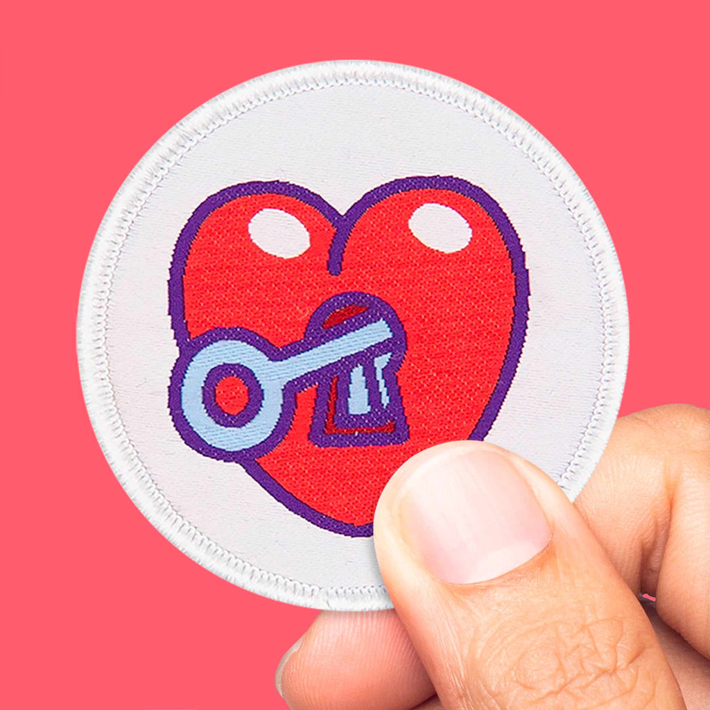 Main tenant un écusson cœur rouge avec clé bleue, patch thermocollant coloré pour vêtements ou sacs