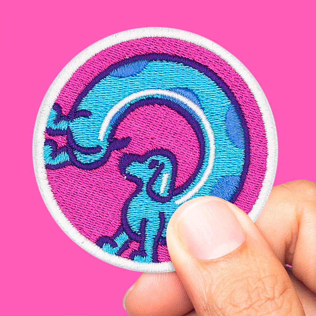 Main tenant un écusson thermocollant ou scratch représentant un chien saucisse stylisé dans des couleurs vives.