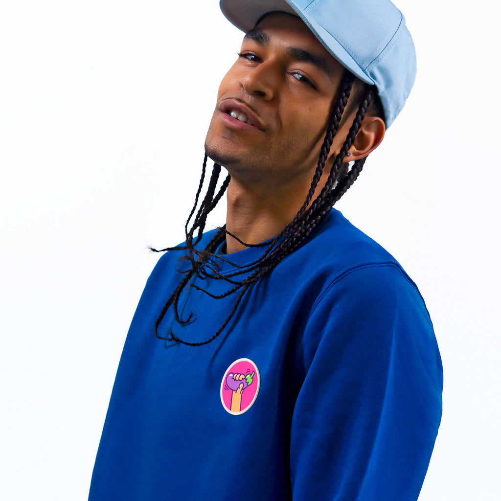 Homme en pull bleu affichant un écusson aubergine coloré, disponible en patch thermocollant ou scratch.