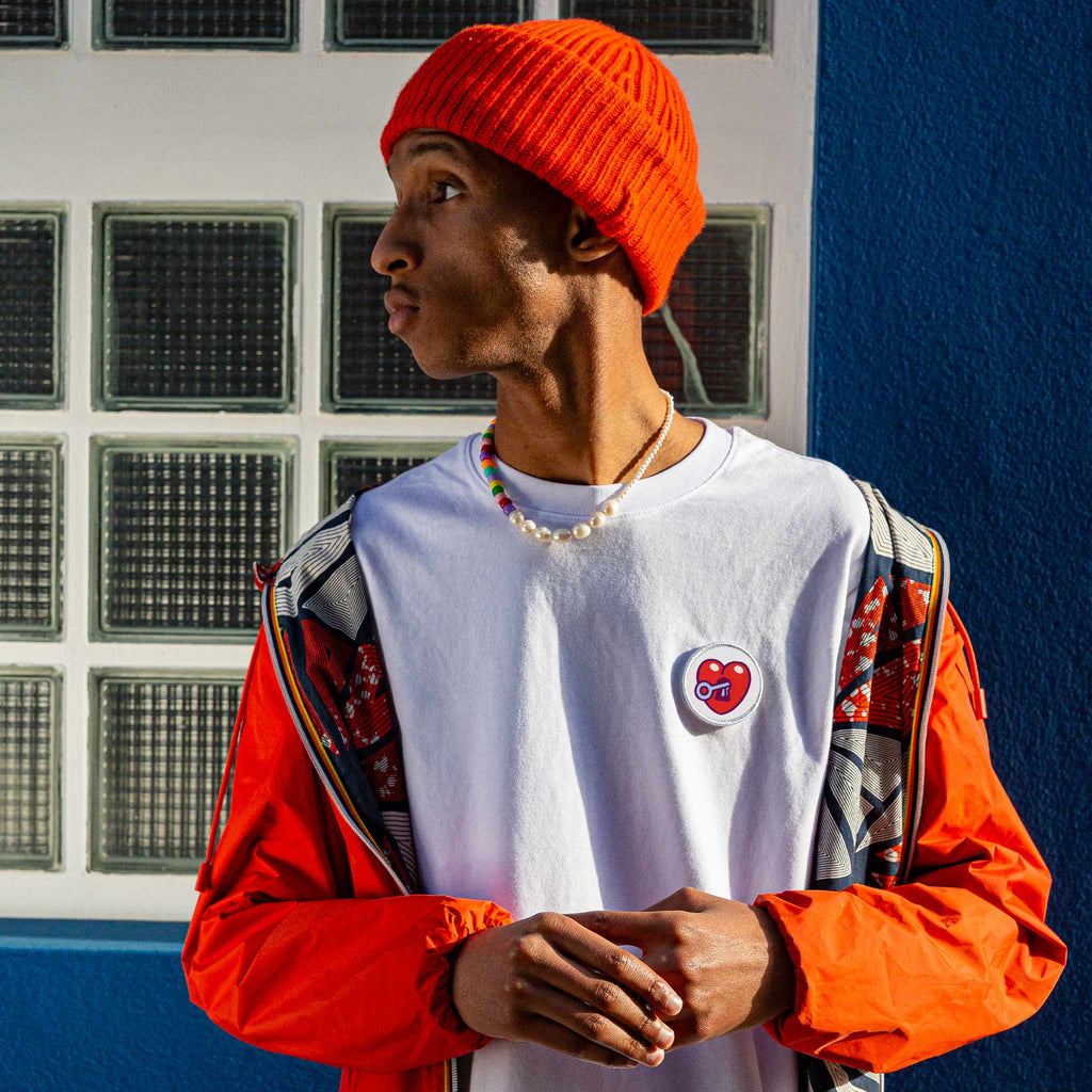 Portrait d’un homme stylé avec bonnet orange, portant un patch cœur rouge scratché sur son t-shirt