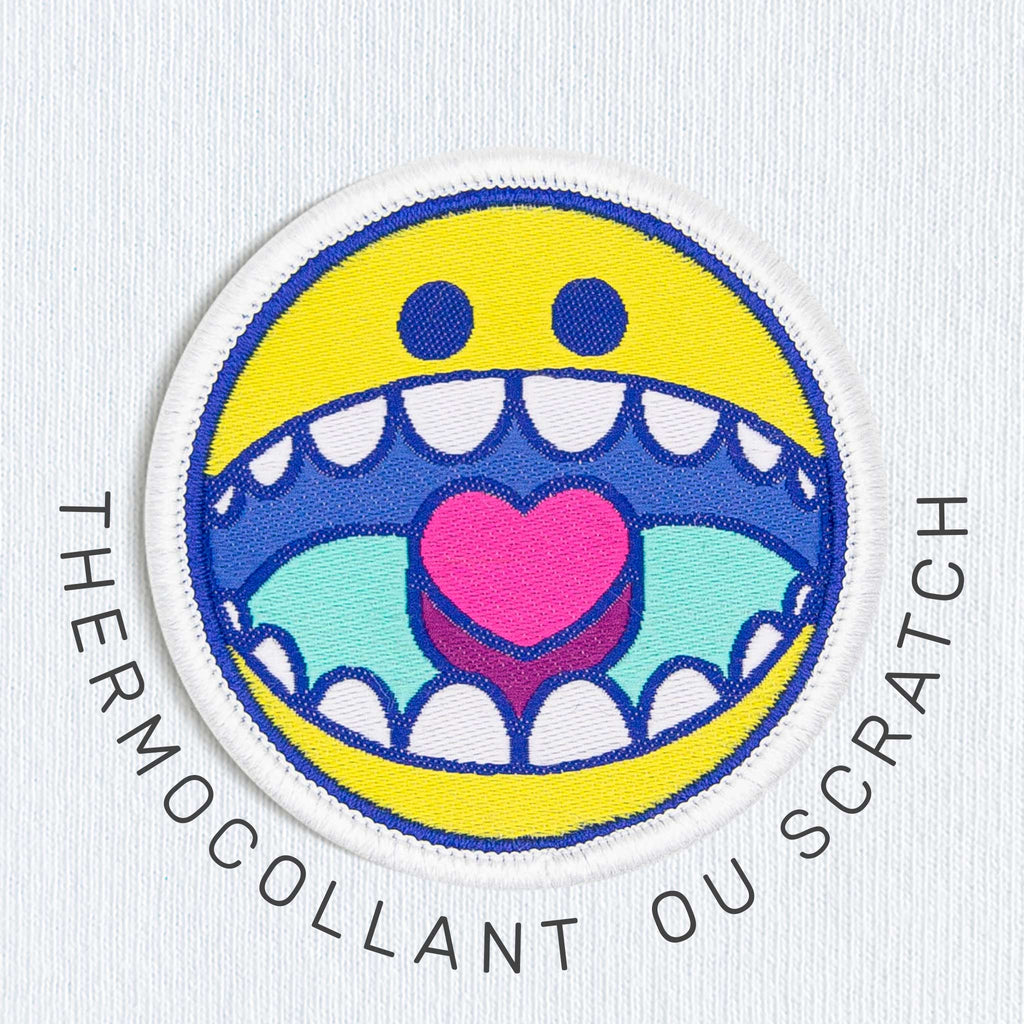 Modèle portant un t-shirt blanc orné d’un écusson smiley brodé sur la poitrine, vue de face.