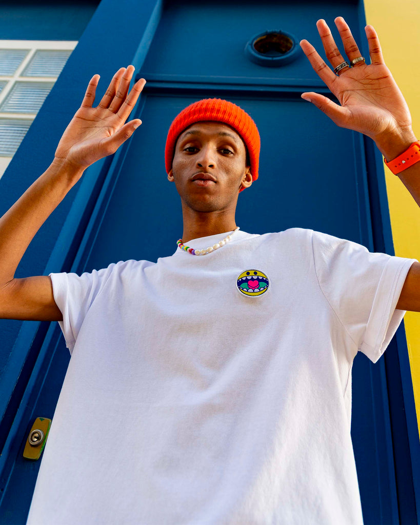 Jeune modèle posant de profil en t-shirt blanc avec un écusson smiley circulaire brodé.
