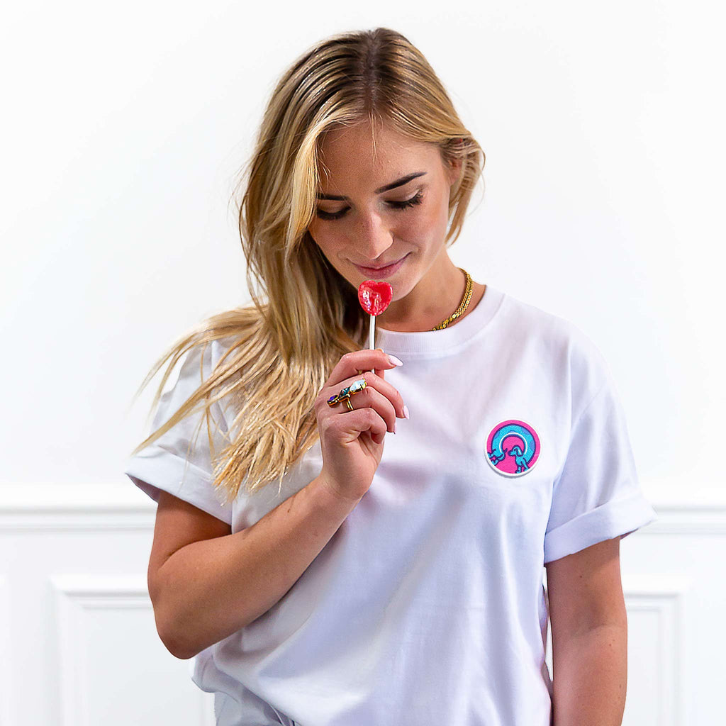 Femme portant un t-shirt blanc avec un écusson scratch chien saucisse en rose et bleu, look décontracté et joyeux.