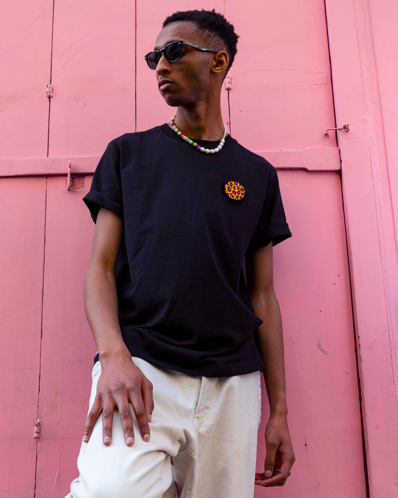 Pose urbaine d'un homme en extérieur avec t-shirt noir et écusson léopard rose de forme circulaire