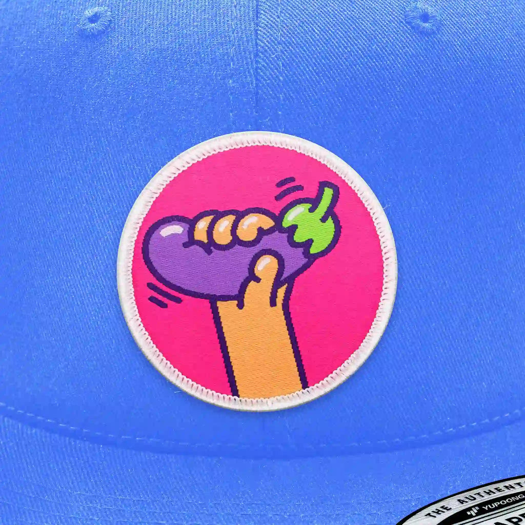 Casquette bleu clair avec écusson thermocollant main serrant une aubergine violette.