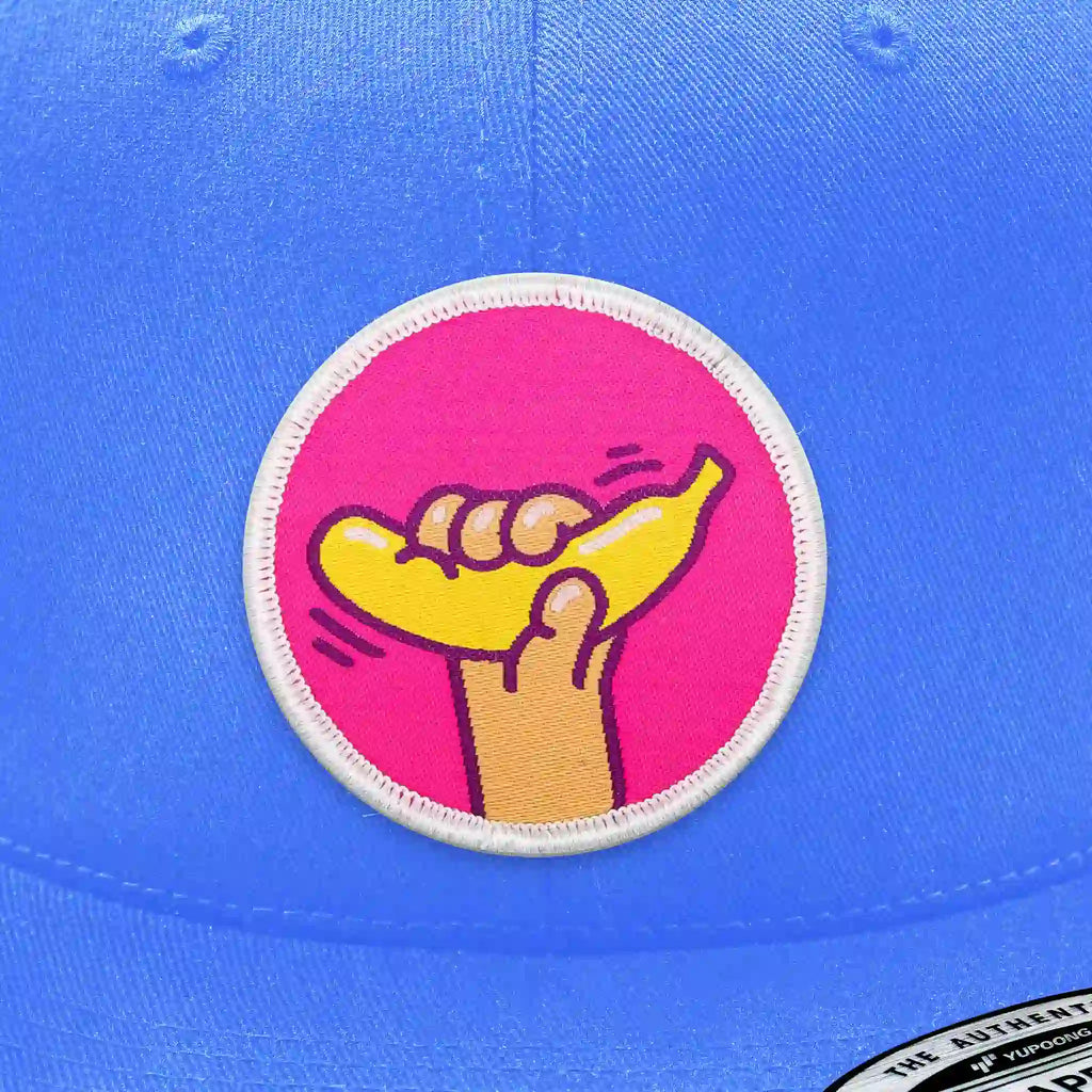 Casquette bleu clair avec écusson thermocollant main tenant une banane jaune.