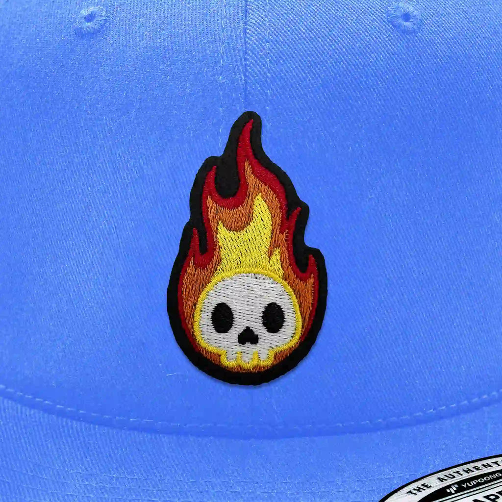 Casquette bleu clair avec écusson thermocollant phosphorescent flamme rouge et jaune avec crâne blanc.