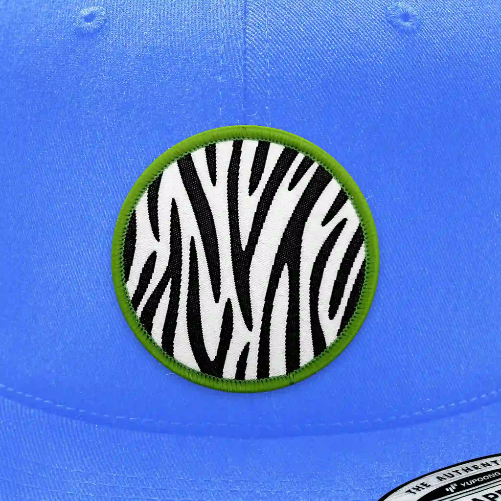 Casquette bleu clair avec écusson thermocollant rond imprimé en motif zèbre noir et blanc avec bordure verte, style jungle.