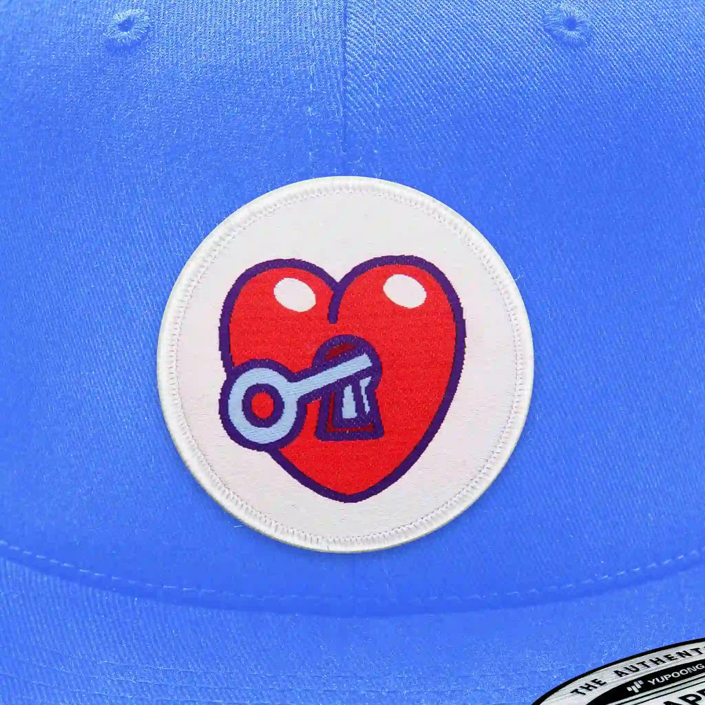 Casquette bleu clair avec écusson thermocollant rond en forme de cœur rouge avec serrure et clé, symbole cœur à prendre.