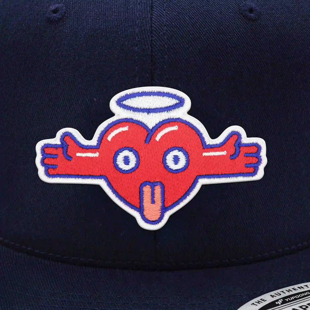 Casquette Flexfit bleue navy snapback avec écusson brodé en forme de cœur rouge avec des bras, une auréole et une expression fun, casquette streetwear personnalisable avec velcro et écussons interchangeables.