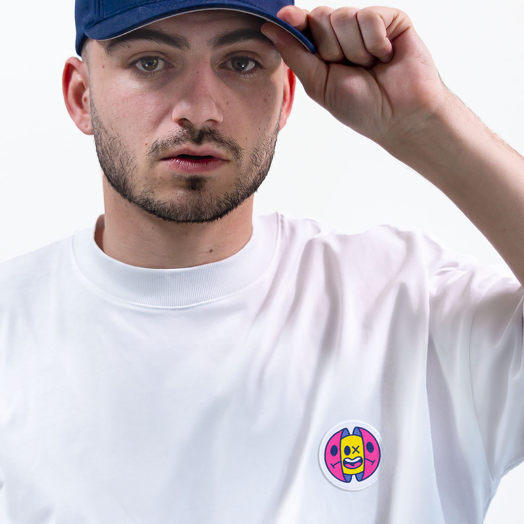 Homme avec une casquette portant un super t-shirt en coton bio avec un écusson sourire positionné sur le cœur