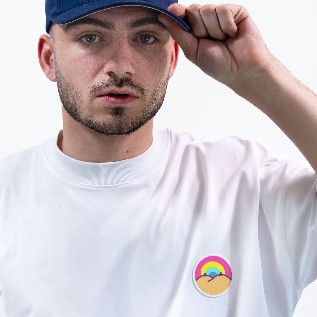 Homme avec une casquette portant un super t-shirt en coton bio avec un écusson arc-en-ciel positionné sur le cœur